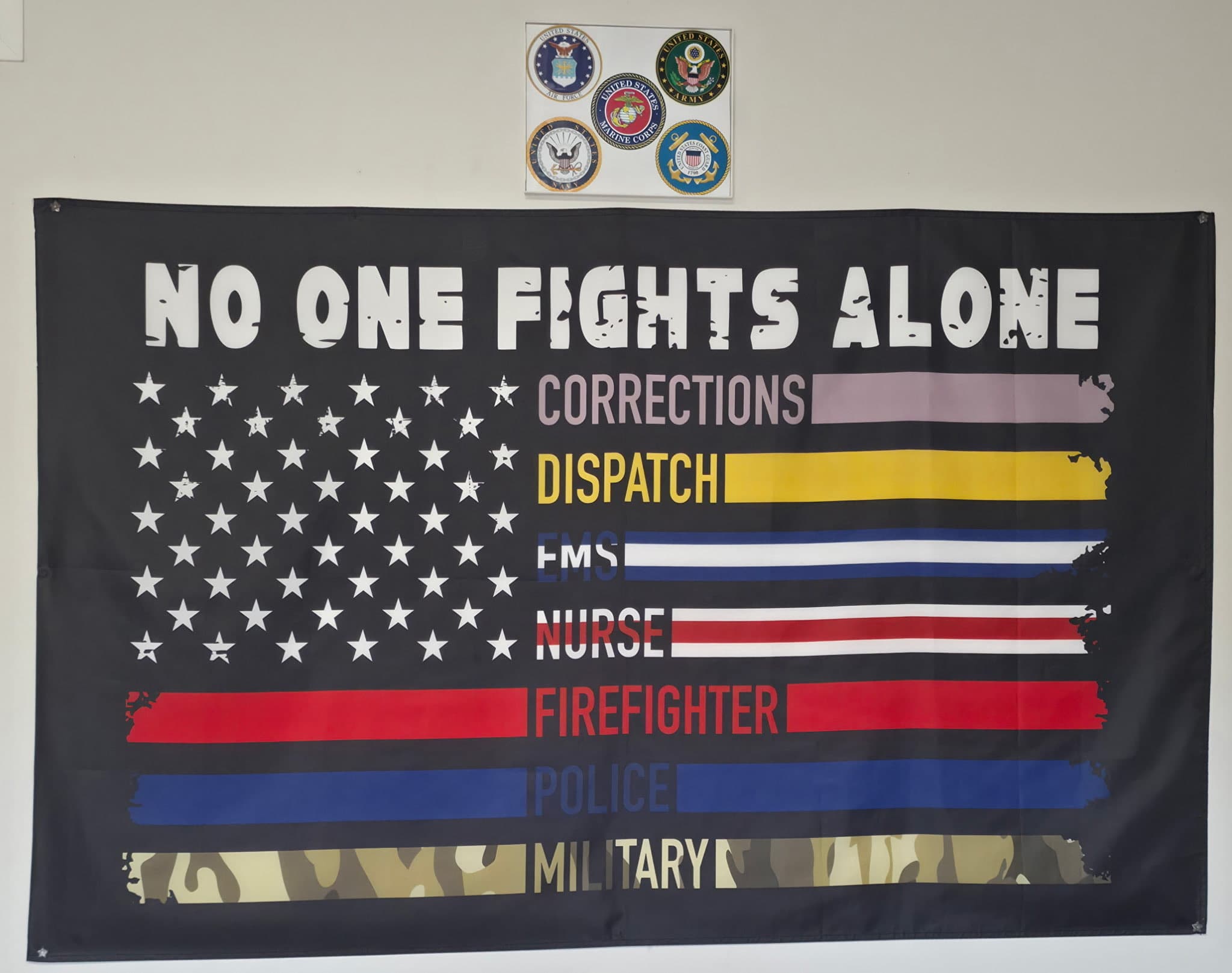 'No One Fights Alone' banner hanging inside the TVI shop, honoring Corrections, Dispatch, EMS, Nurses, Firefighters, Police, and Military